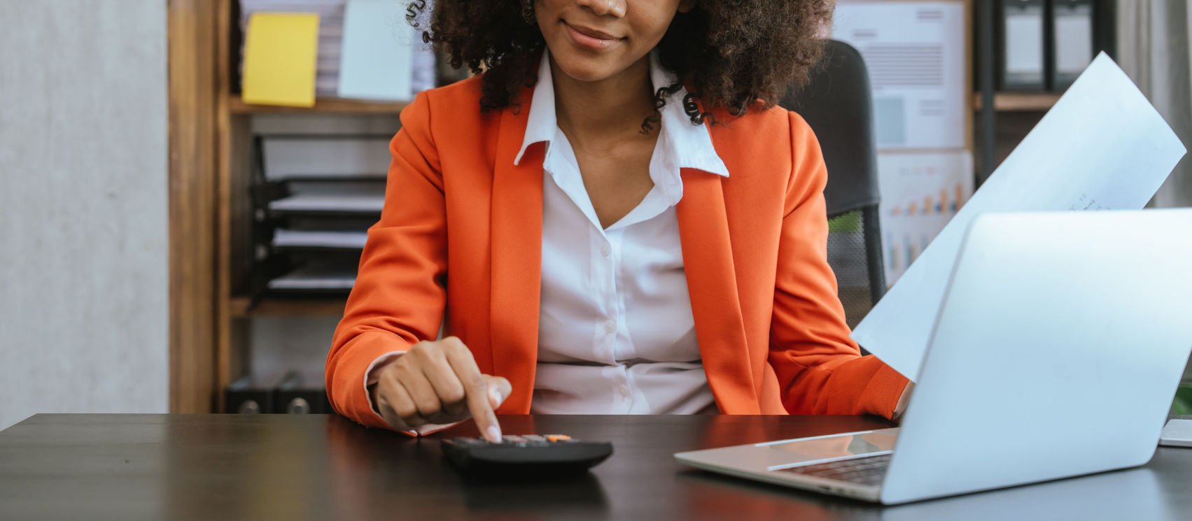 Woman typing on calculator in orange suit jacket